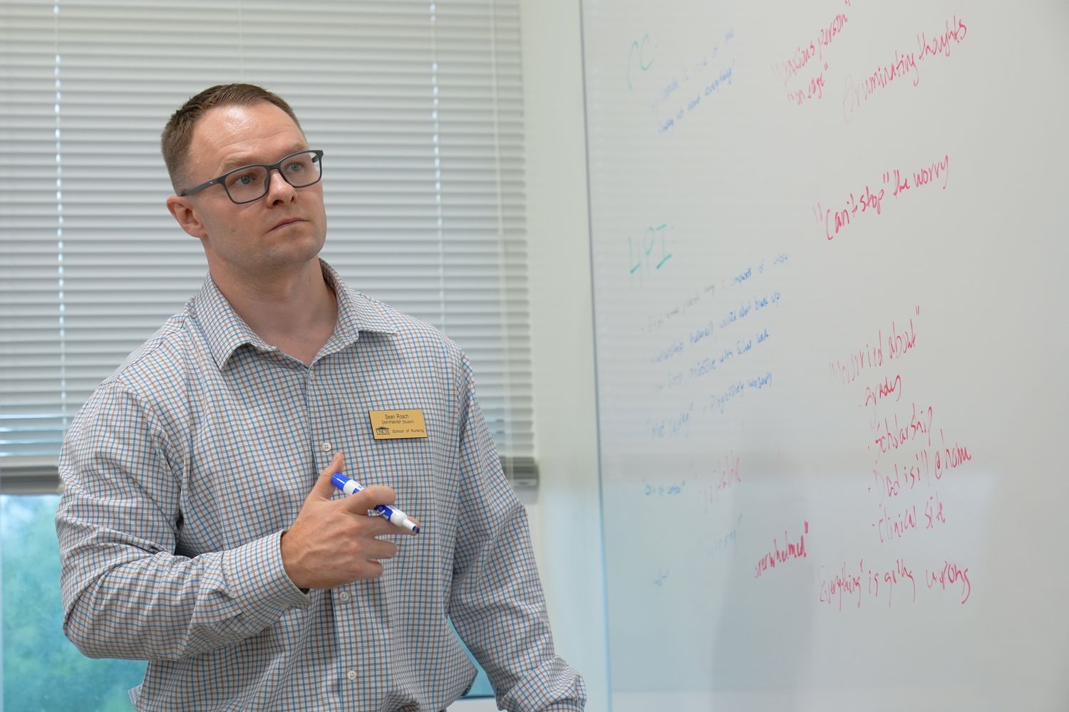 A Psychiatric Mental Health DNP student looks at a white board covered in notes about their practice simulation client. 