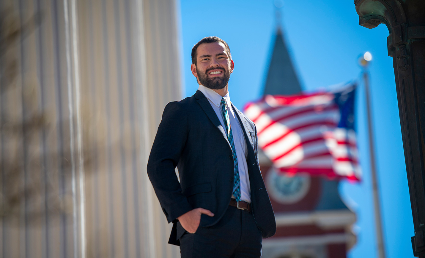 male student in a suit with American flag flying in background