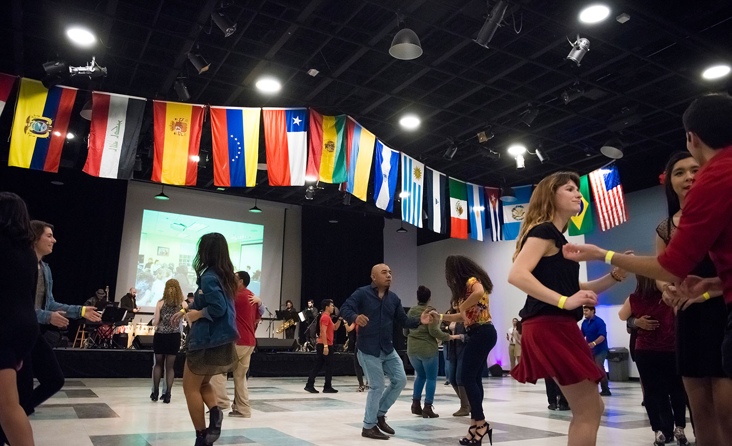 A group of salsa dancers in front of a large screen with world flags hanging from above
