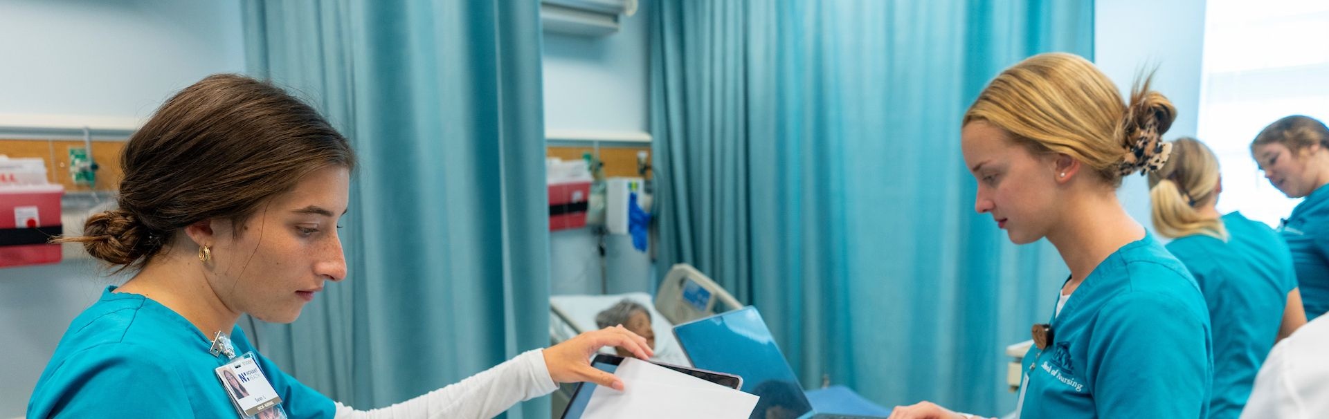 Two nursing students in scrubs examine charts in the Simulation Lab